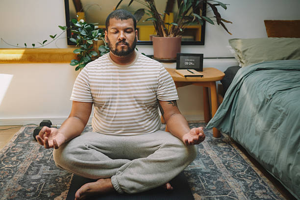 A man sitting cross-legged on a patterned rug meditating with his hands in gyan mudra