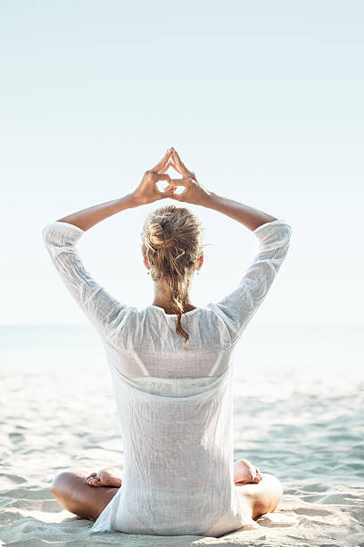 Young woman sitting on the  beach and meditating. Balancing the energy in yoga style. Sea in background.